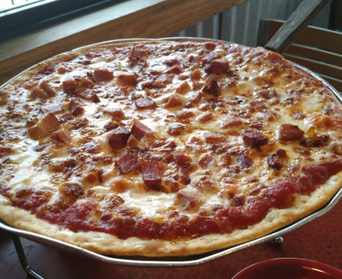 A freshly baked pizza with a golden crust, topped with cheese, chunks of ham, and a rich tomato sauce.
