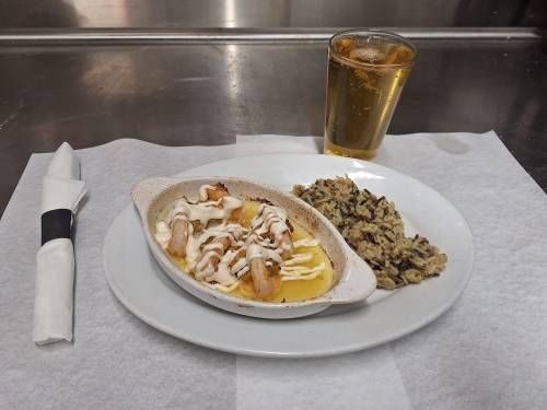 A plate with shrimp in sauce, rice, and a glass of beer on a white napkin.