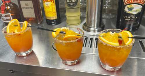 Three colorful cocktails with orange slices and cherries, garnished with black straws, on a bar counter.