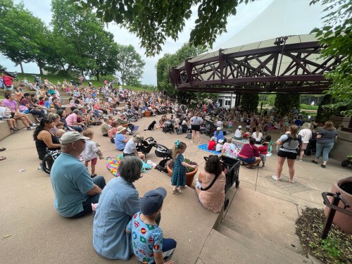 A large crowd gathers on steps at an outdoor event, with families and children enjoying the atmosphere.