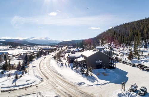 A snowy mountain town with buildings, trees, and a clear blue sky, showcasing a serene winter landscape.