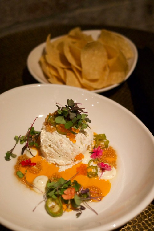 A creamy dish garnished with herbs and edible flowers, served with a side of tortilla chips.
