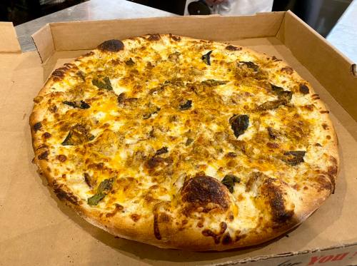 A freshly baked pizza with a golden crust, topped with cheese and green herbs, in a pizza box.