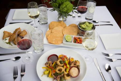 A beautifully arranged table with various dishes, including appetizers, guacamole, and colorful main courses, surrounded by drinks.