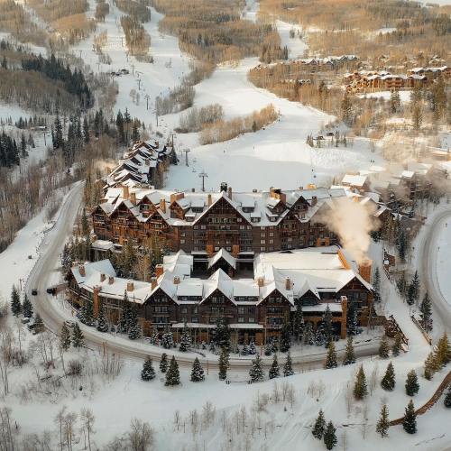 Aerial view of a snow-covered resort surrounded by trees and ski slopes, with smoke rising from the building.