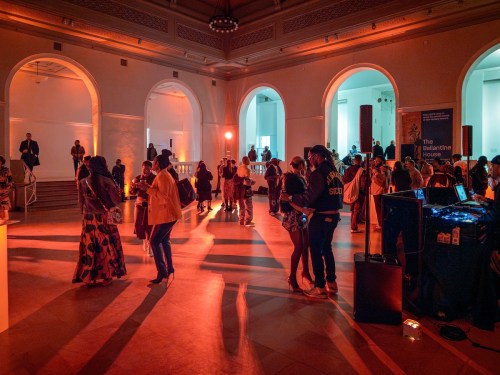 A lively event scene with guests mingling, dancing, and enjoying the atmosphere in a warmly lit venue.