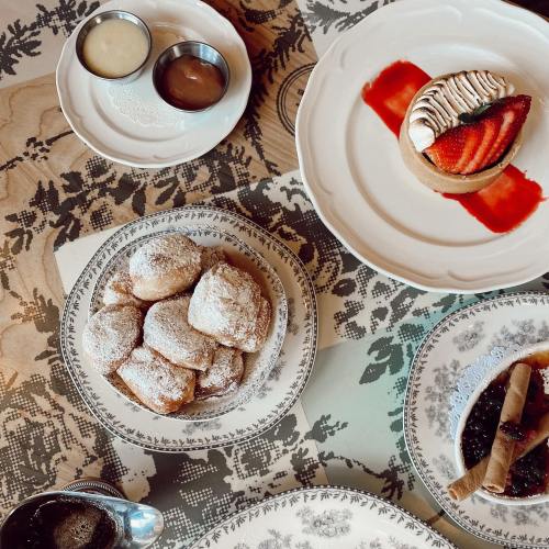 A table spread with desserts: powdered sugar pastries, a tart with strawberries, and dipping sauces in small bowls.