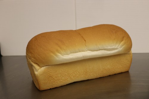 A loaf of fresh, golden-brown bread with a soft, fluffy top resting on a metallic surface.