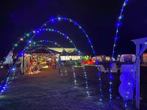 A festive scene with colorful lights, decorated trees, and holiday displays under a night sky.
