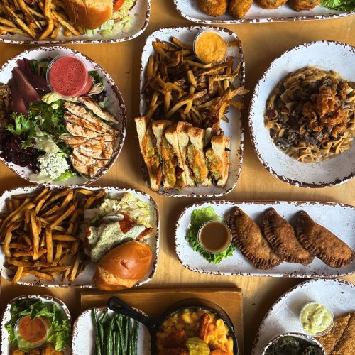 A variety of dishes including sandwiches, fries, salads, pasta, and dips arranged on a table.