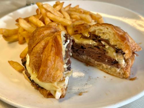 A croissant sandwich filled with beef and cheese, served with a side of golden French fries on a white plate.