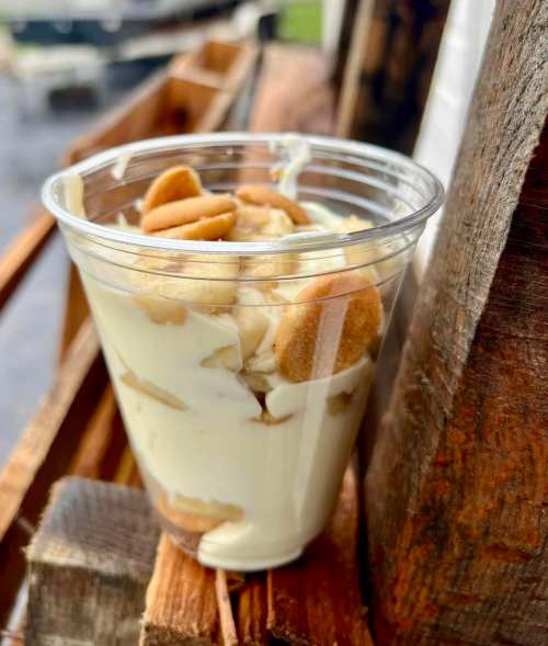 A clear cup filled with layered dessert, featuring creamy filling and cookie pieces, resting on a wooden surface.
