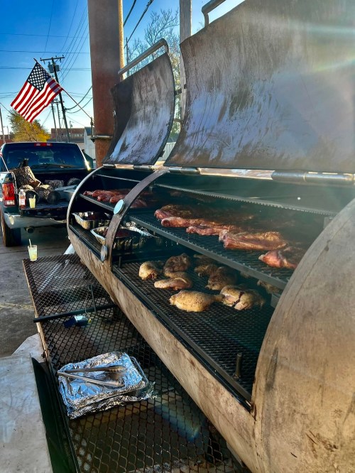A large grill with various meats cooking, set outdoors with an American flag in the background.