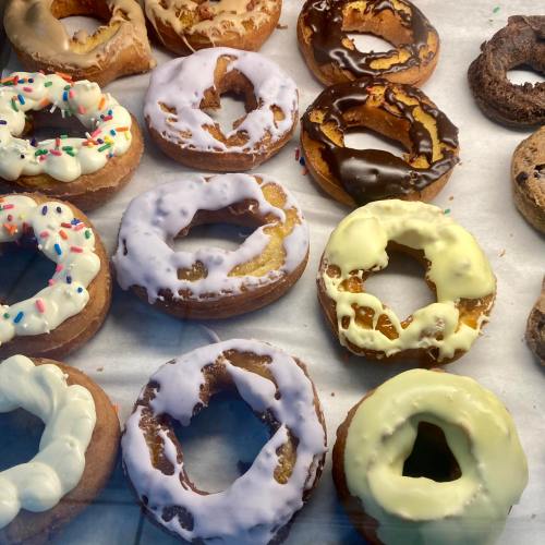 A variety of colorful donuts with different toppings, including sprinkles, chocolate, and cream, arranged on a display.