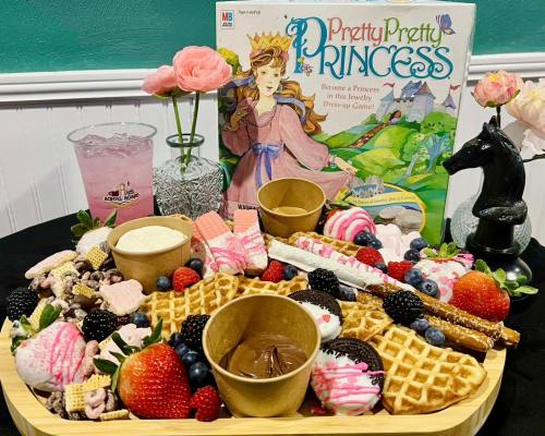 A colorful dessert platter with waffles, berries, candies, and ice cream, alongside a "Pretty Pretty Princess" game box.