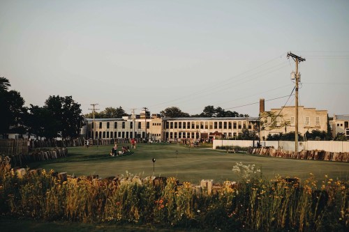 A scenic view of a grassy area with wildflowers, surrounded by historic buildings and power lines at sunset.