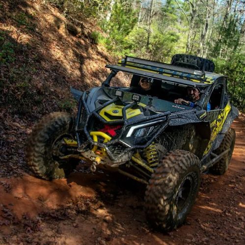 A rugged off-road vehicle navigating a dirt trail surrounded by trees in a forested area.