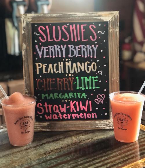 A chalkboard menu displays four slushie flavors: Very Berry, Peach Mango, Cherry Lime Margarita, and Straw-Kiwi Watermelon.