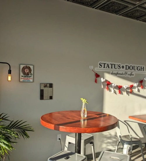Cozy café interior with a wooden table, a vase, and wall decor featuring "Status Dough" and a weather report.