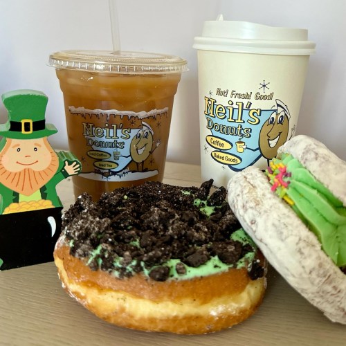 A festive display featuring a donut with mint frosting, a coffee cup, iced drink, and a leprechaun cutout.