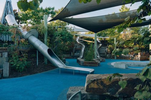 A modern playground featuring metal slides, shaded areas, and lush greenery.