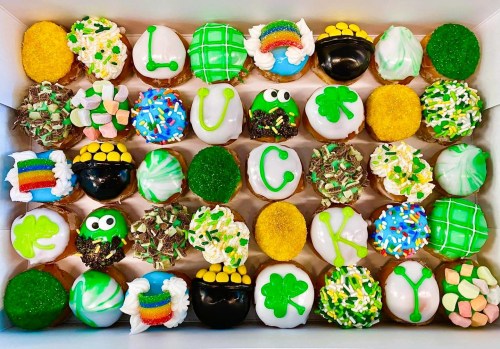 A colorful assortment of decorated cupcakes in a box, featuring green, gold, and festive St. Patrick's Day themes.