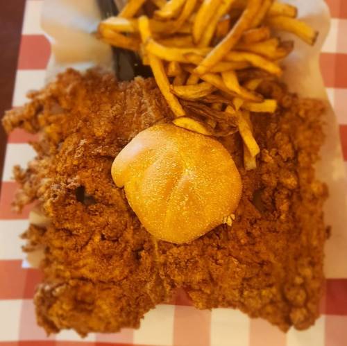 A plate of crispy fried chicken with a soft bun and a side of golden French fries on a checkered paper.