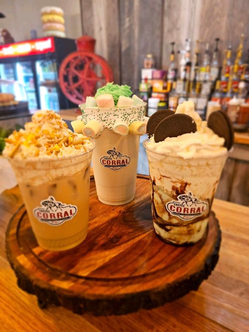 Three colorful milkshakes topped with whipped cream, sprinkles, and cookies, served on a wooden platter.