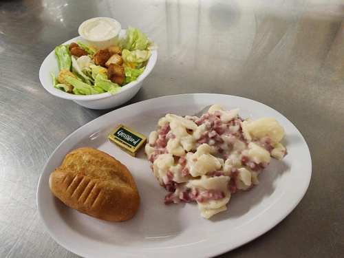 A plate with mashed potatoes and a roll, alongside a bowl of salad with dressing and fried chicken pieces.