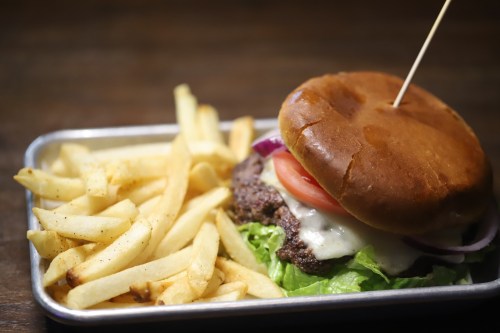 A juicy burger with lettuce, tomato, and cheese, served with a side of crispy French fries on a metal tray.
