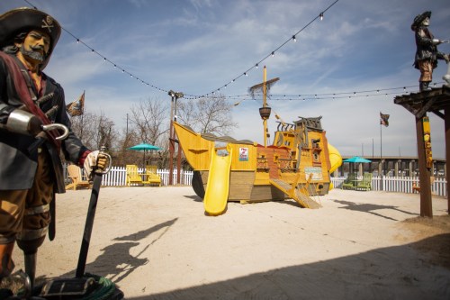 A pirate-themed playground featuring a large yellow ship, slide, and pirate statues in a sandy area.