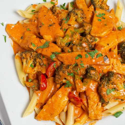 Creamy pasta dish with chicken, broccoli, and red peppers, garnished with fresh parsley on a white plate.