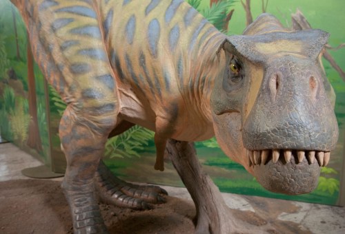 A detailed dinosaur model with a textured body and fierce expression, set against a green jungle backdrop.