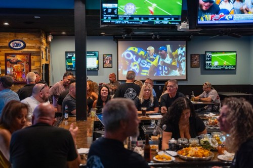 A lively sports bar scene with patrons enjoying food and drinks, watching games on multiple screens.