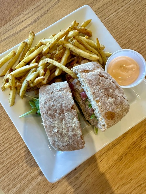 A sandwich cut in half on a plate, served with fries and a small cup of dipping sauce.