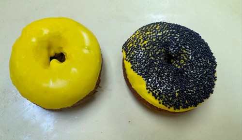 Two donuts: one with bright yellow icing and the other with yellow icing topped with black sprinkles.