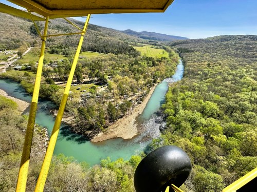 Aerial view of a winding river surrounded by lush greenery and hills under a clear blue sky.