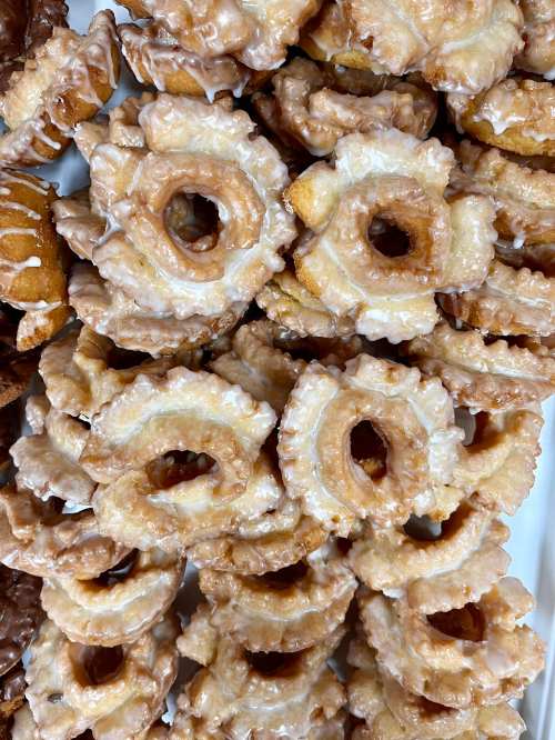 A close-up of glazed donuts arranged in a pile, featuring a unique ring shape with a textured surface.