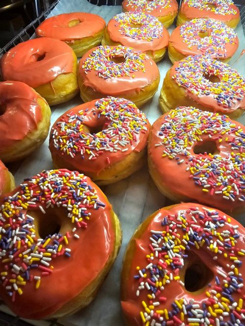 A tray of freshly baked donuts with bright orange icing and colorful sprinkles on top.