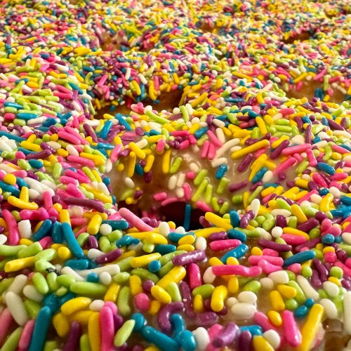 A close-up of colorful donuts covered in vibrant sprinkles in various shades of pink, green, and blue.