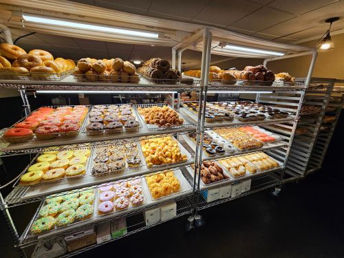 A display of various baked goods, including donuts, pastries, and bagels, arranged on metal shelves in a bakery.
