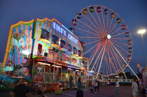 A vibrant carnival scene at dusk featuring a colorful circus ride and a brightly lit Ferris wheel.