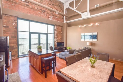 Modern loft with exposed brick walls, large windows, and a stylish kitchen island, featuring a cozy living area.