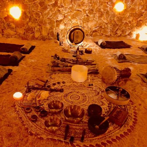 A serene room with stone walls, featuring mats on the sand and various musical instruments arranged on a decorative rug.