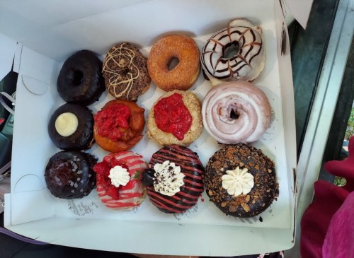 A box of twelve assorted donuts, featuring various toppings like chocolate, sprinkles, fruit, and cream.