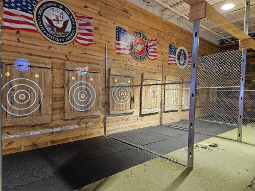 Indoor target range with wooden walls, multiple target boards, and safety netting, featuring military and American flags.