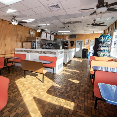 Bright, empty diner interior with orange and blue tables, wooden walls, and a counter in the background.