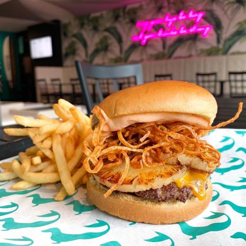 A delicious burger topped with crispy onions and cheese, served with a side of golden fries on a patterned table.