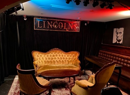 A cozy lounge with vintage furniture, a sign reading "LINCOLN'S," and a portrait of Abraham Lincoln on the wall.
