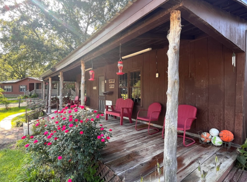 A rustic porch with red chairs, surrounded by blooming roses and sports equipment, under a sunny sky.